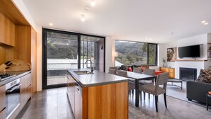 A modern kitchen with a large island, a dining area with patterned chairs, a fireplace, and a TV mounted on the wall.