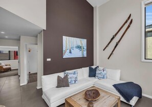 Una sala de estar moderna con un sofá blanco, una mesa de centro y un cuadro de un paisaje nevado.