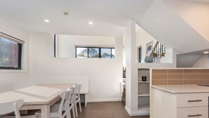 A modern kitchen with a dining area, a built-in dishwasher, and a view through a window. - Blues Air 4 - Woodridge (Woodridge)
