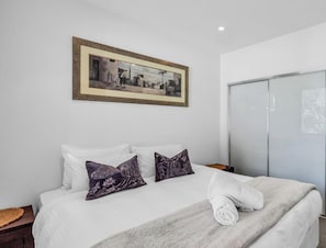Una habitación de hotel con cama, almohadas, una colcha, una toalla, un cuadro y un armario.