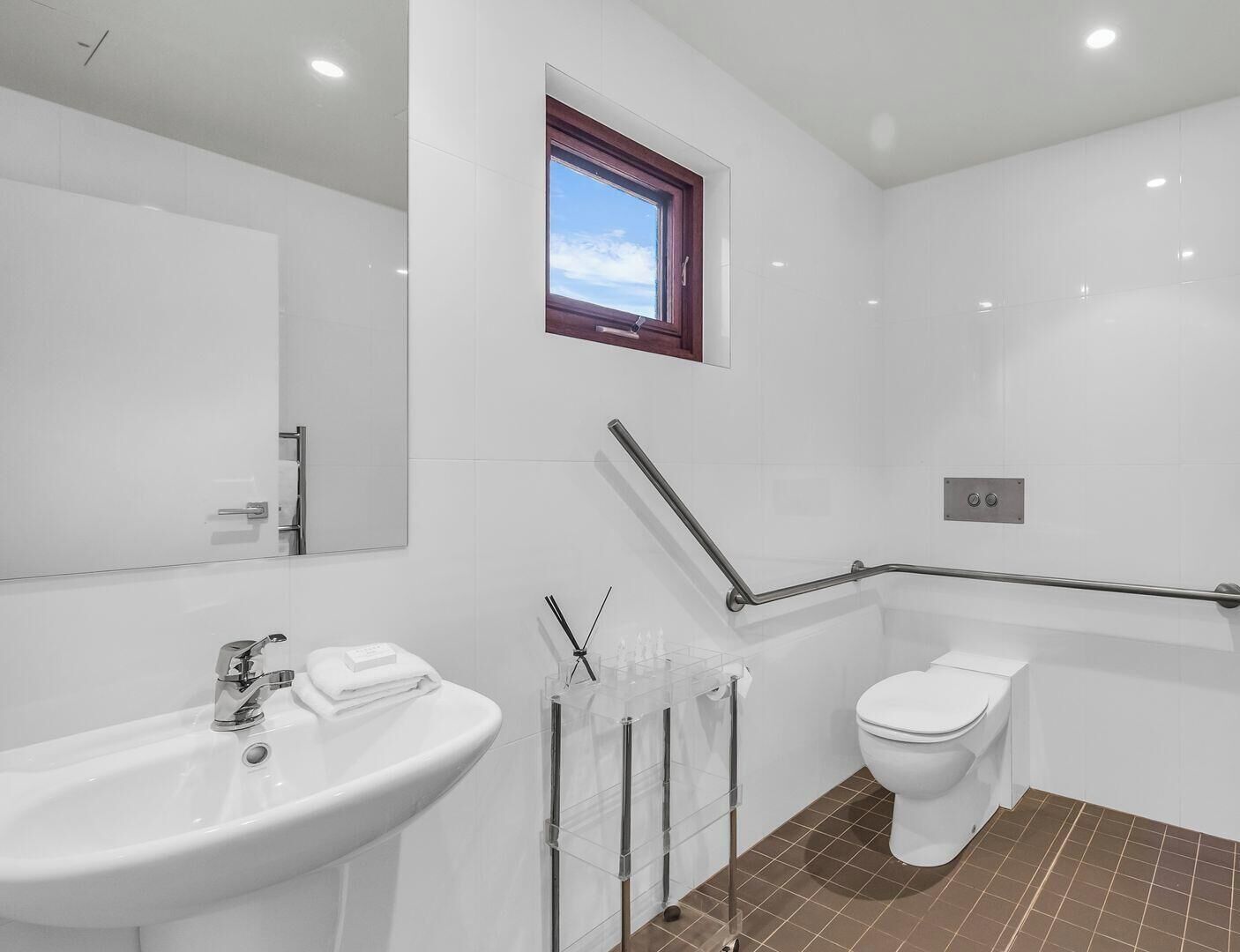 Ein modernes Badezimmer mit einem großen Spiegel, einem Waschbecken, einer Toilette und einem Fenster.