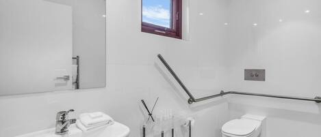 Ein modernes Badezimmer mit einem großen Spiegel, einem Waschbecken, einer Toilette und einem Fenster.