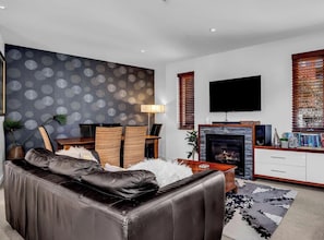 Un salon moderne avec un canapé en cuir, une cheminée, un téléviseur à écran plat et une bibliothèque.