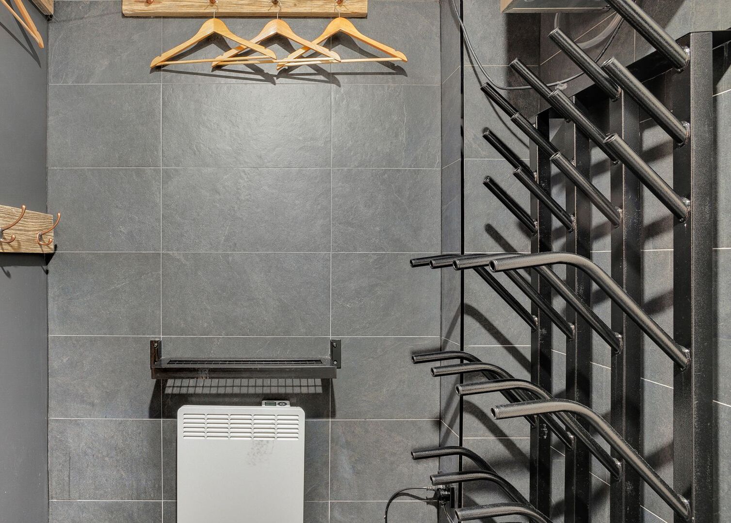 A tiled wall with a radiator, wooden hangers, and a metal rack.