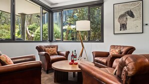 Een kamer met leren banken, een ronde houten tafel en een groot raam met uitzicht op groen.