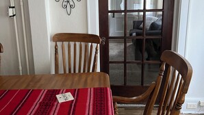 Un coin repas avec une table et des chaises en bois, un chemin de table rouge à motifs et un élément décoratif mural.