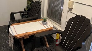 Un petit espace extérieur aménagé avec une table en bois et deux chaises Adirondack noires.