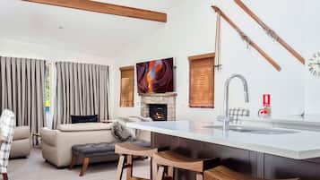A modern kitchen with a central island, a stone fireplace, and a large window with blinds.