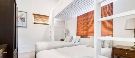 A bedroom with two beds, wooden blinds, a bedside table with a lamp, and a framed picture on the wall.