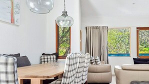 Ein modernes Wohnzimmer mit Esstisch, Sofa und zwei mit Vorhängen versehenen Fenstern.