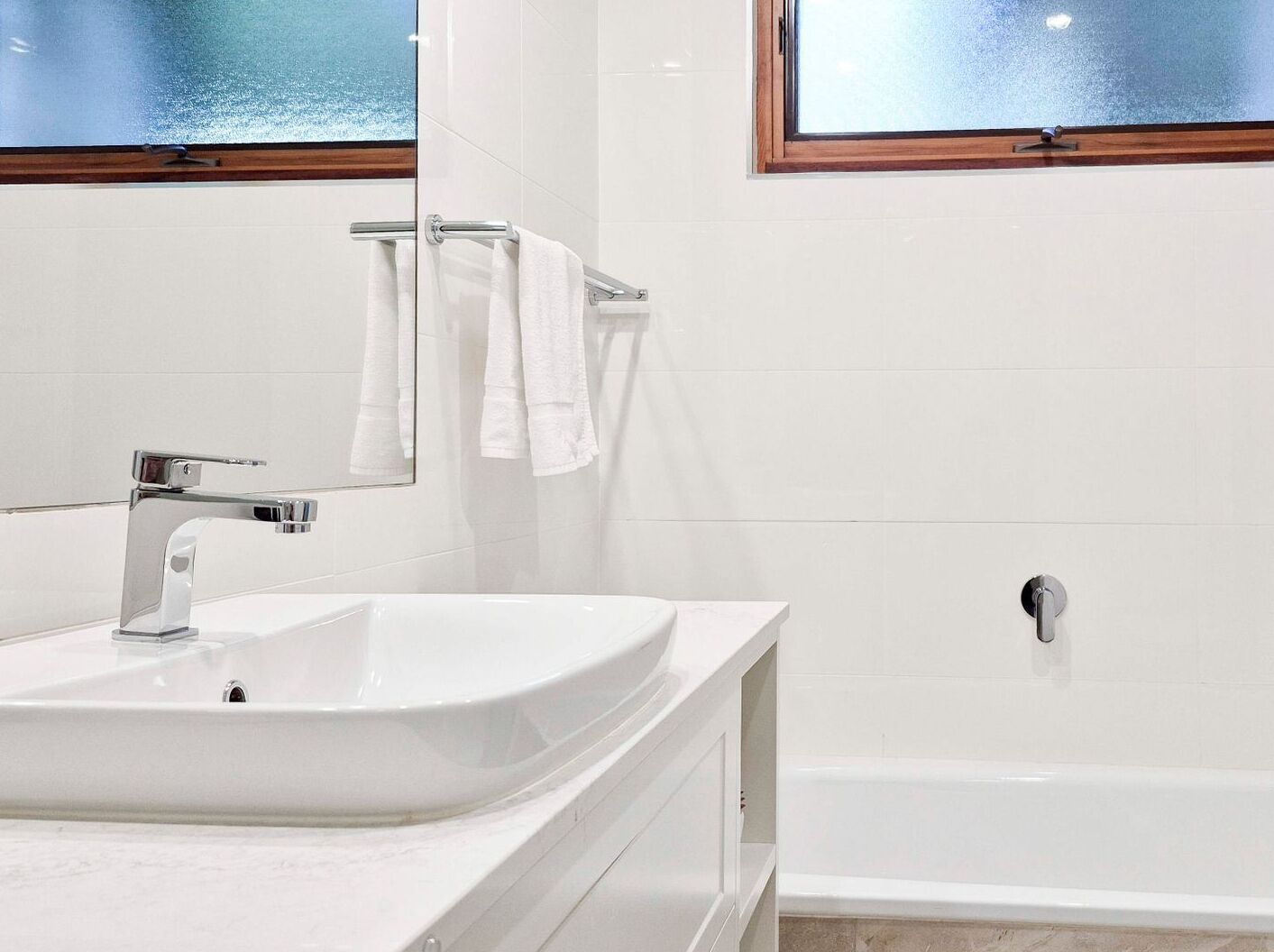 Ein modernes Badezimmer mit einem weißen Waschbecken, einer Duschkabine aus Glas und einem Fenster über der Dusche.
