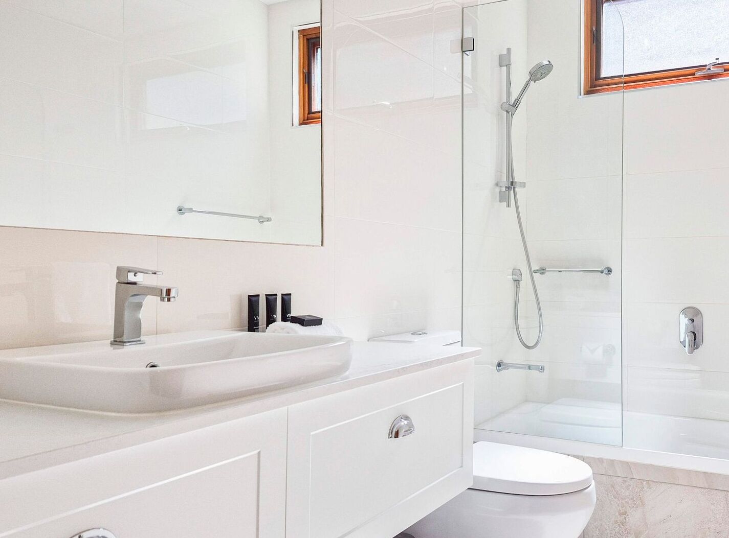 A modern bathroom with a white sink, mirror, and glass shower enclosure.
