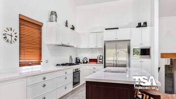 A modern kitchen with white cabinetry, a stainless steel refrigerator, a built-in oven, and a coffee machine.