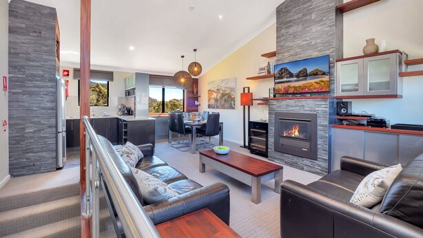 A modern living room with a fireplace, leather sofas, a dining area, and a kitchen visible through an open door.