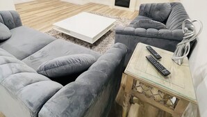 A modern living room with grey sofas, a white coffee table, a fireplace, and a flat-screen TV mounted on the wall. - Modern Thorold Apt w/ Pool Table (Thorold)