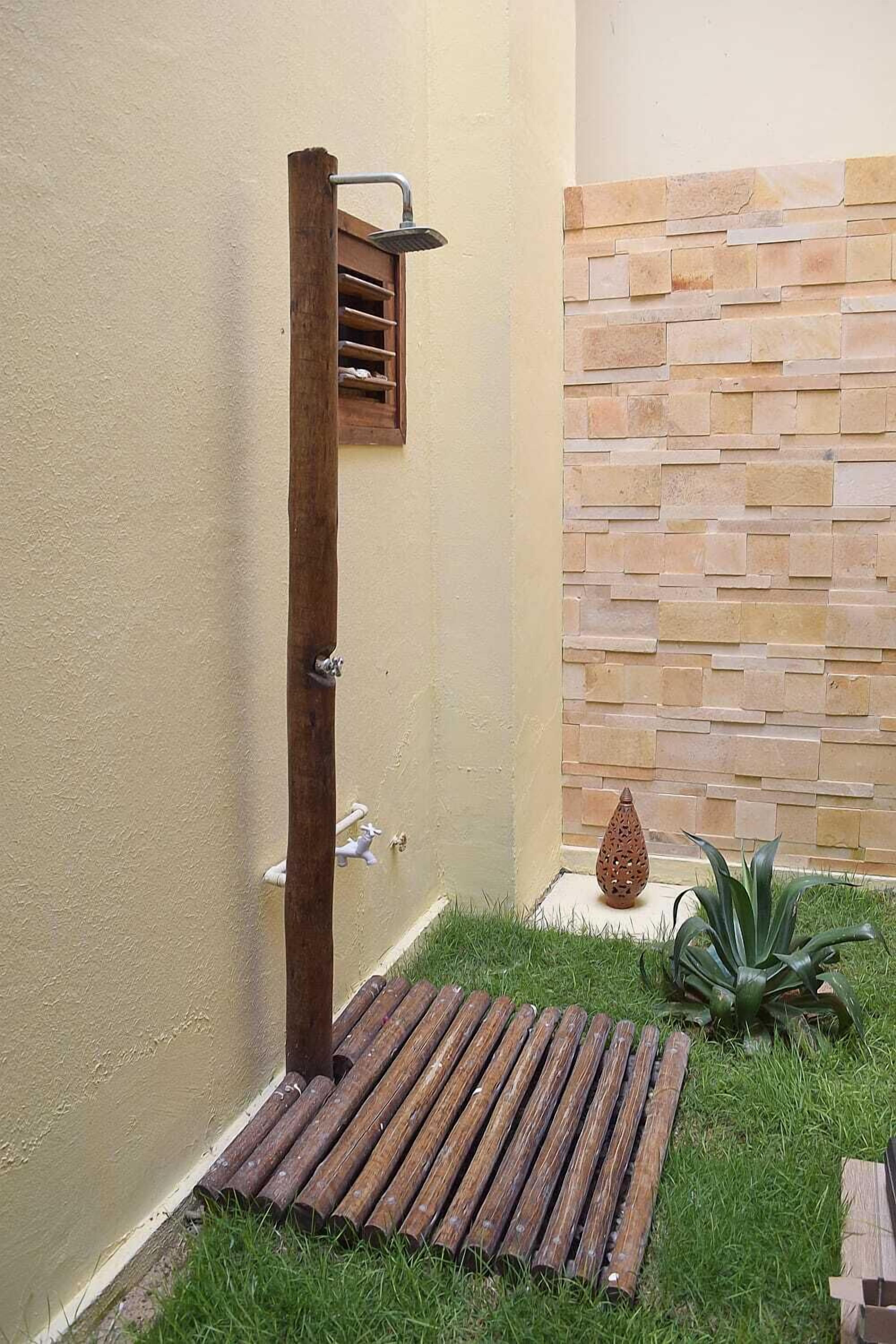 Un box de ducha de madera con un muro de piedra de fondo, una planta pequeña y una pieza decorativa de piedra.