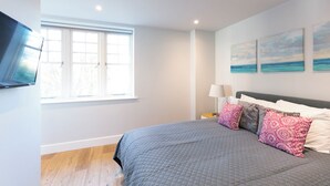 Un dormitorio con cama, ventana, televisor y obras de arte en la pared.