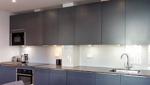 Una cocina moderna con armarios oscuros, horno empotrado, microondas, lavamanos y tostadora.