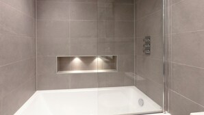 Un box de ducha moderno con puerta de cristal, repisa integrada y panel de control en la pared.