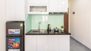 Cocina compacta con armarios blancos, encimera negra, pileta de acero inoxidable y refrigerador negro con etiqueta Funiki.