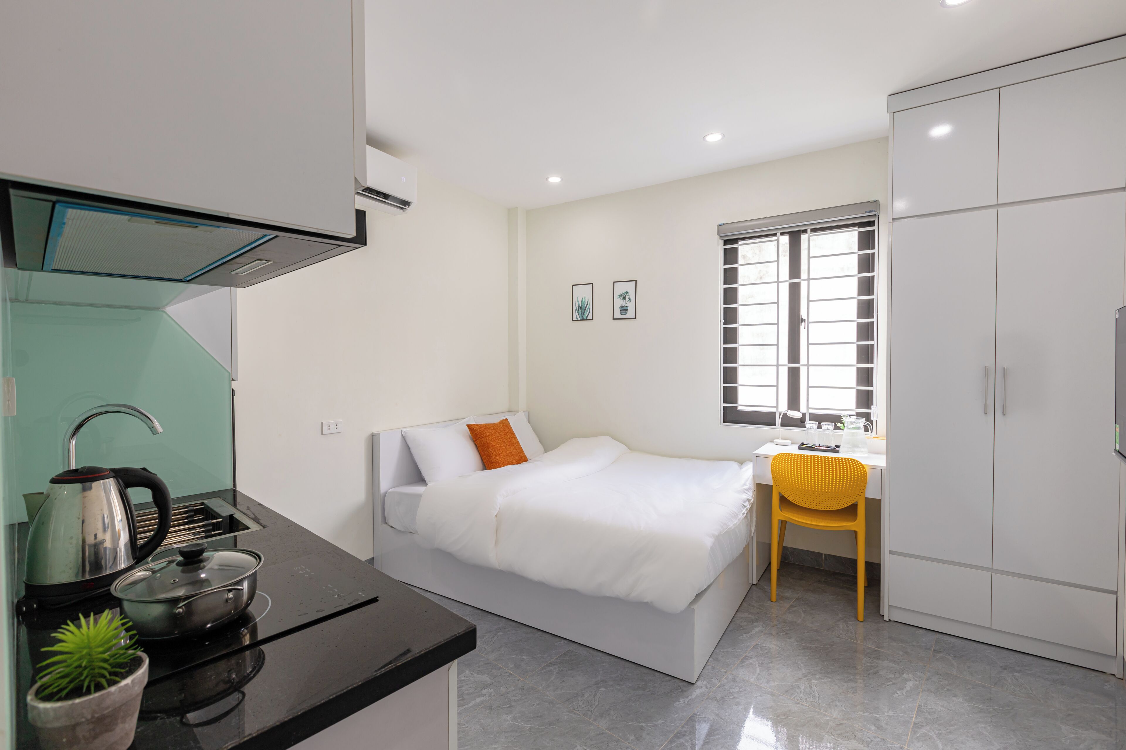 Una habitación compacta con cama, escritorio pequeño, silla, kitchenette y armario.