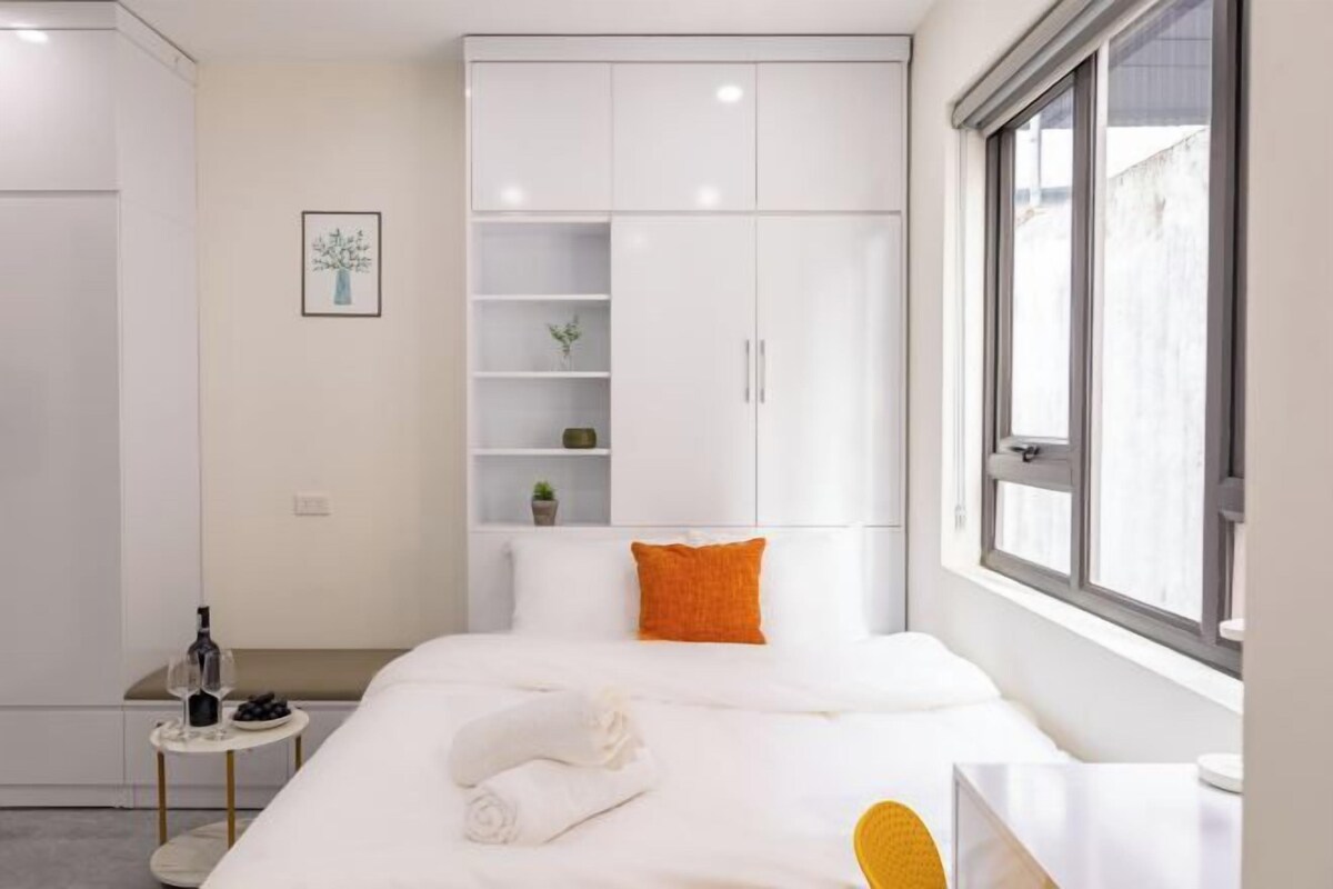 A modern hotel room with a large bed, a bedside table, a wardrobe, and a window with a view.