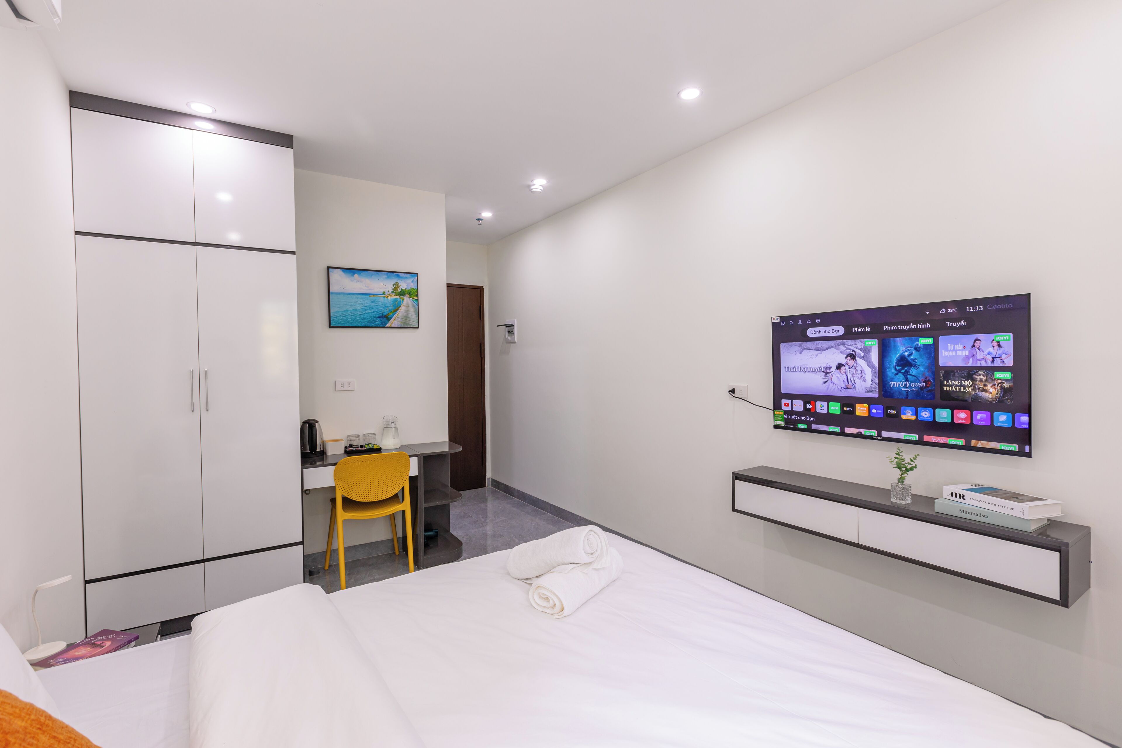 A hotel room with a bed, a desk, a chair, a TV, and a wardrobe.