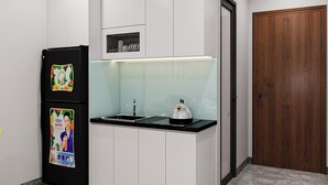 Una cocina compacta con muebles blancos, un refrigerador negro, un lavamanos de acero inoxidable y una puerta de madera.