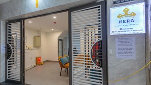 Entrada de un hotel con un letrero que dice "HERA HOTEL & APARTMENT" e información de contacto.
