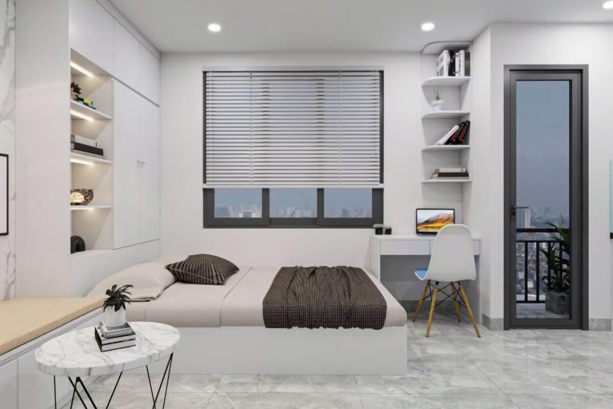 Ein modernes Schlafzimmer mit Bett, Nachttischen, einem Schreibtisch und einem Stuhl. Ein Fenster mit Jalousien, ein Bücherregal und eine Tür zu einem Balkon sind ebenfalls vorhanden.
