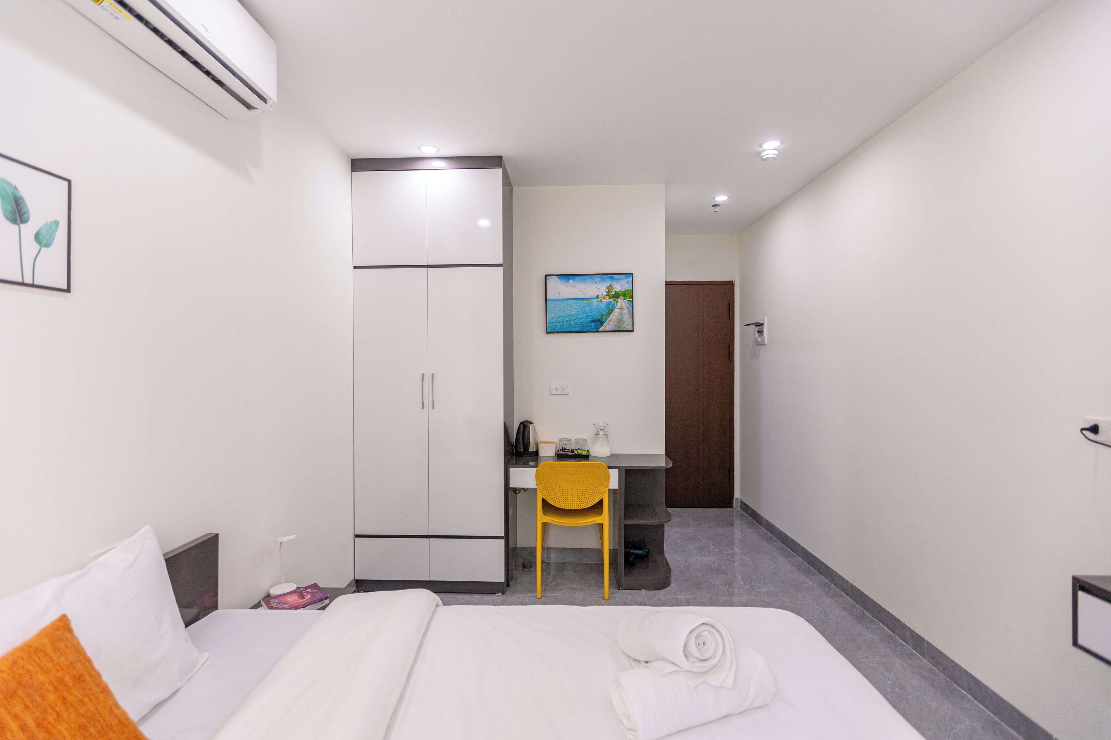 Habitación de hotel con cama, escritorio, silla, armario y un cuadro en la pared.