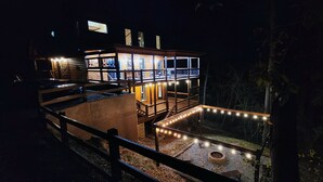 Eine zweistöckige Holzhütte mit einer verglasten Veranda, Lichterketten und einer Feuerstelle.