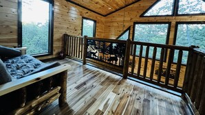 Ein Blockhaus-Interieur mit Holzwänden und Holzböden, einem Bett mit Kopfteil, einer Bank und einem Geländer mit Wald-Silhouette.