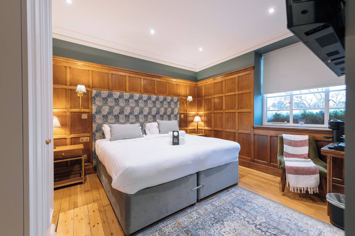 Un dormitorio con una cama grande, paneles de madera, una ventana con vistas y un escritorio con una silla.