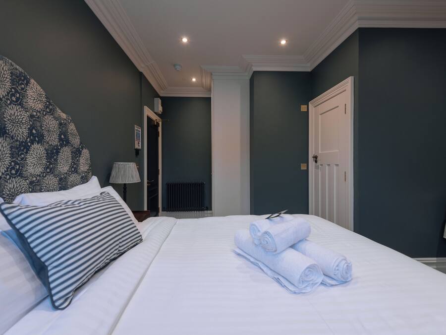 A hotel room with a large bed, a headboard with a floral pattern, and a neatly made bed with rolled towels.