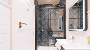 Un baño moderno con ducha de vidrio, azulejos blancos y un espejo grande.