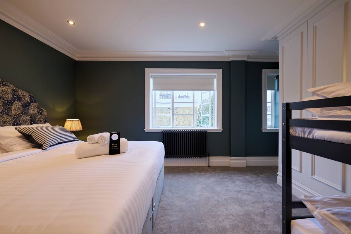 Una habitación de hotel con una cama, un radiador, una ventana y una litera.