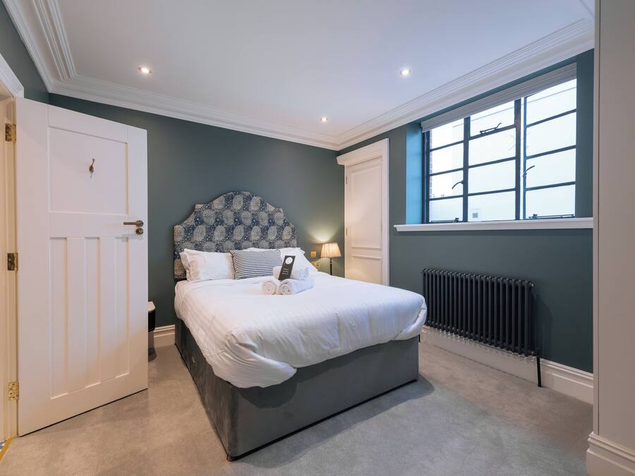A bedroom with a large bed, a headboard with a patterned design, a window with multiple panes, and a radiator.