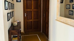 A hallway with a wooden door, a small table with a box, and a mirror on the wall.