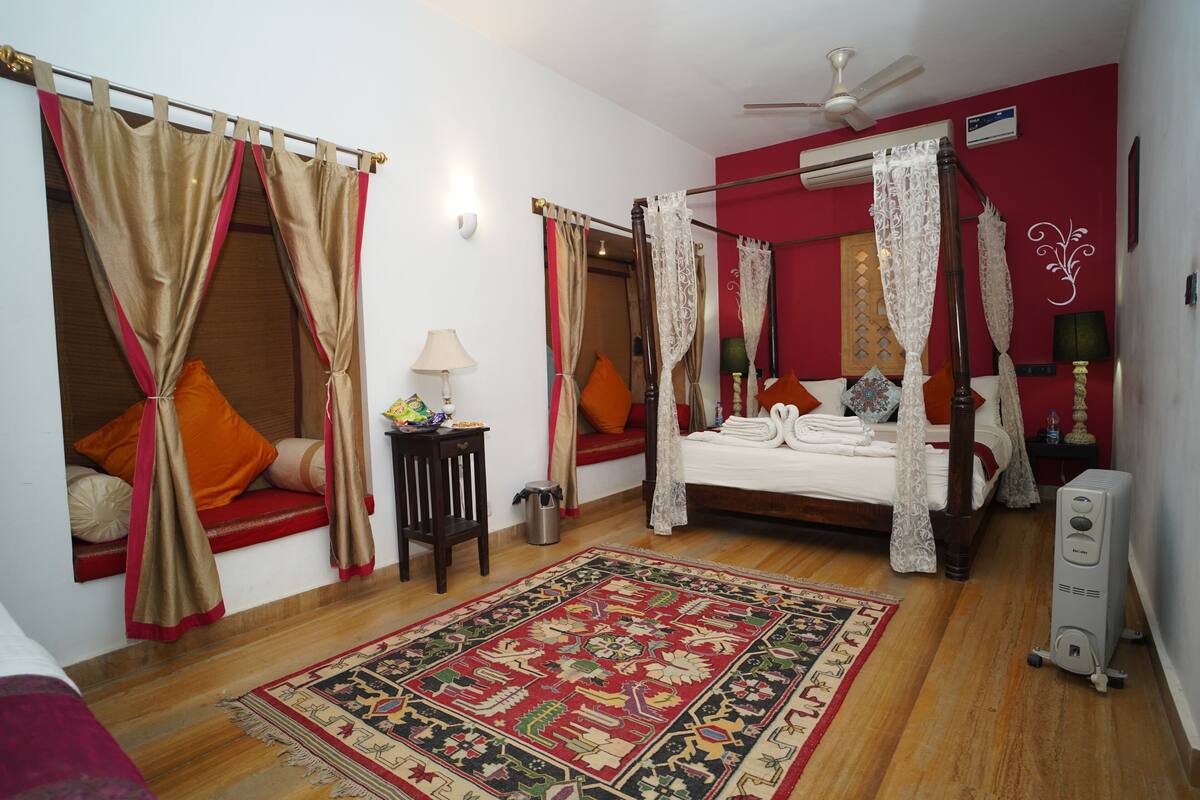 A bedroom with a four-poster bed, a red accent wall, a ceiling fan, and a traditional rug.