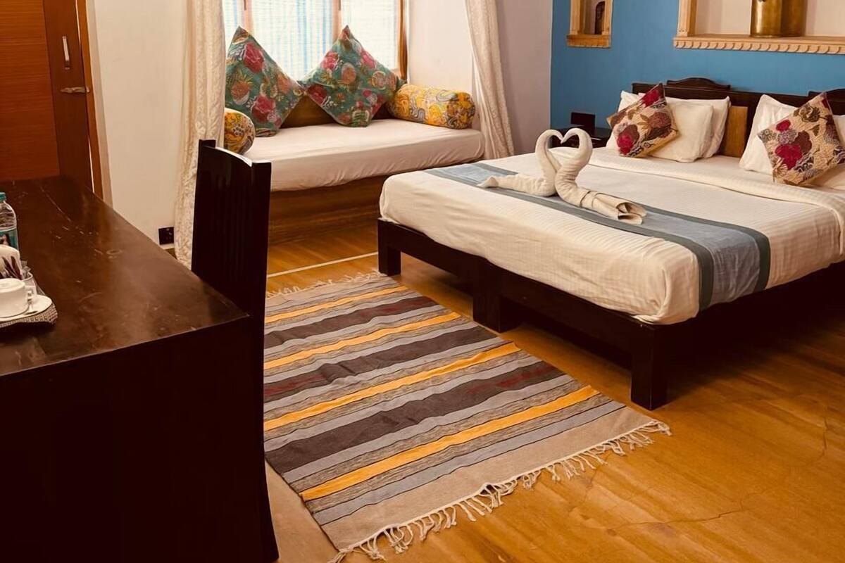 A bedroom with a bed, a window with curtains, a bedside table, and a wooden floor.