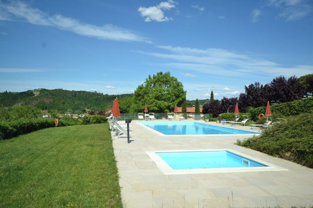 Un espace piscine comprenant deux piscines, entouré d’une pelouse bien entretenue et de parasols rouges.