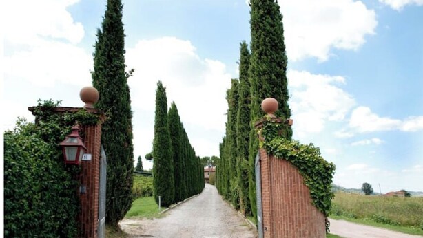 Um caminho ladeado por sebes altas e estreitas e paredes de tijolo com ornamentos esféricos no topo.