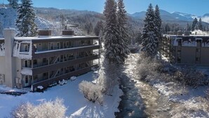 Un hotel de varios pisos con un patio central, rodeado de árboles cubiertos de nieve y un telón de fondo montañoso.