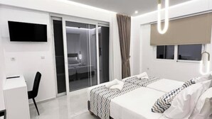 A modern hotel room with a large bed, a desk, a TV, and a sliding door to a balcony. - Luxury Villa (Chania)