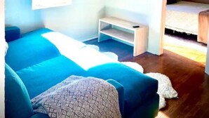 Une chambre à coucher de taille réduite, comprenant un lit, un téléviseur fixé au mur, un petit banc et une fenêtre.