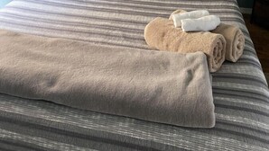 A neatly made bed with striped bedding, a woven throw pillow, and rolled towels on the bed. - Cozy & Historic | Old Bakery Building Close to Downtown (Albuquerque)