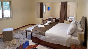 A hotel room with a large bed, a bedside table, a chair, a TV, and a window. - Golf Pyramids View (Giza)