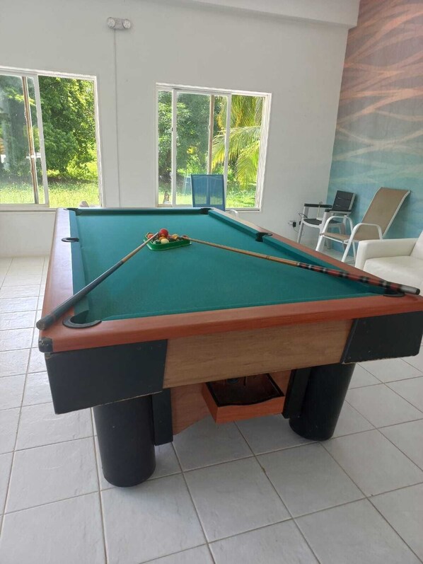 A pool table in a room with large windows, a chair, and a laptop.