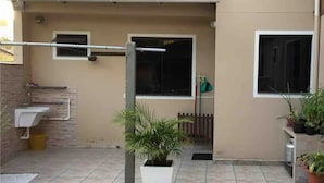 Un patio propre, carrelé, avec un évier blanc, une plante en pot et une fenêtre dont le store est fermé.